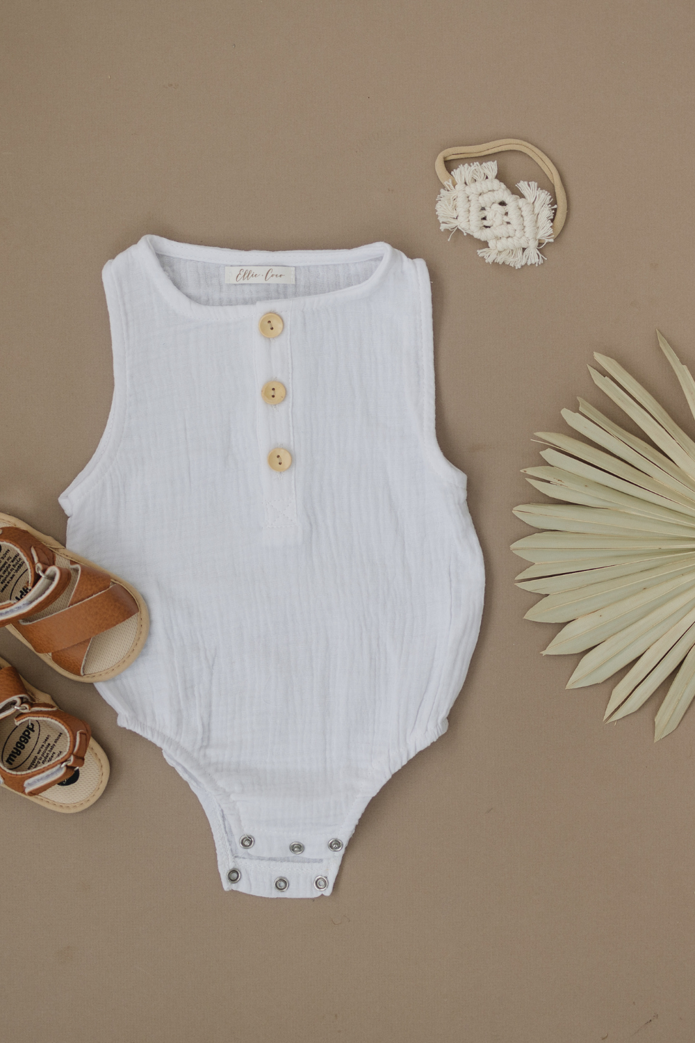 Summer baby outfit with white romper and brown sandals.
