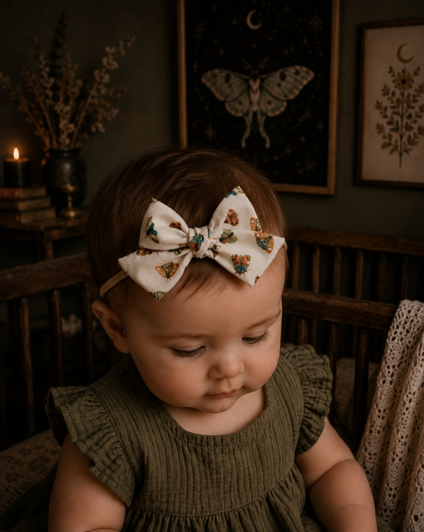 baby girl in a moody nursery wearing a moth patterned baby bow headband