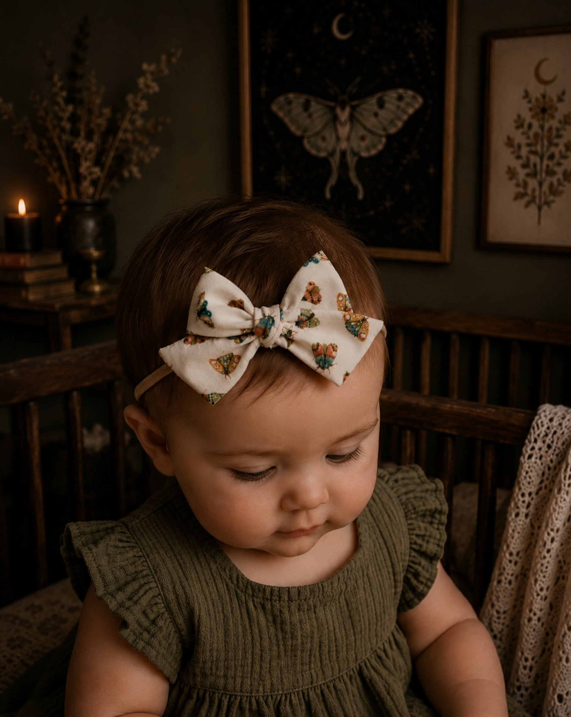 baby girl in a moody nursery wearing a moth patterned baby bow headband